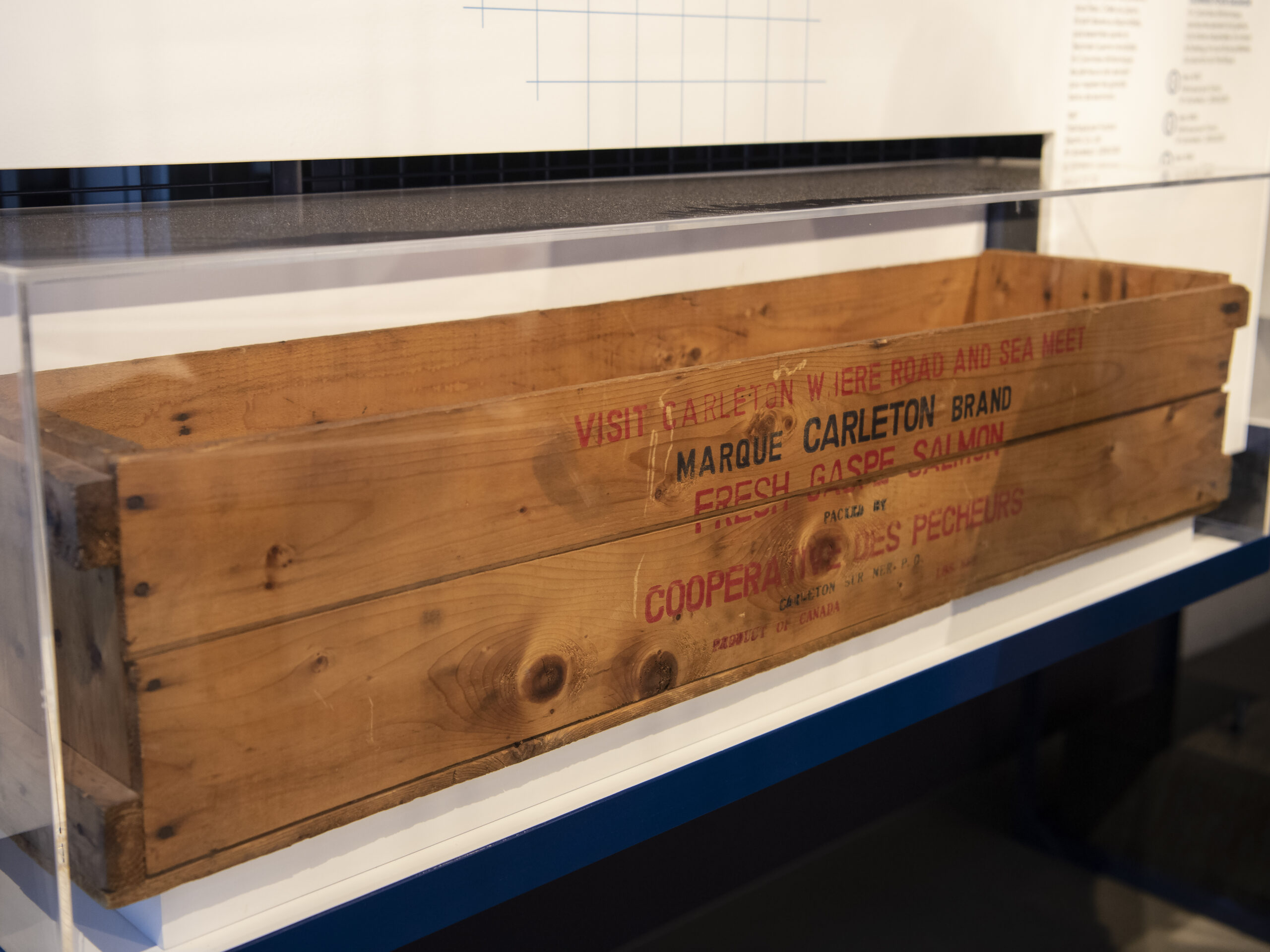 A large, wooden crate. On the side, stenciled lettering has several phrases, including “Fresh Gaspe Salmon packed by Cooperative des pecheurs”