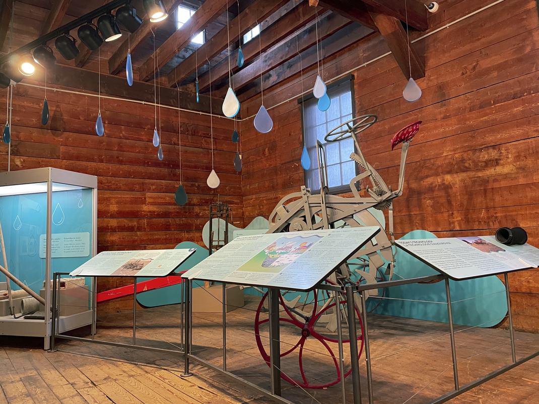 An display at the Canada Agriculture and Food Museum featuring water management. There are interpretive panels and agriculture equipment  on display. Artistic raindrops are hung from the ceiling of the wooden barn.