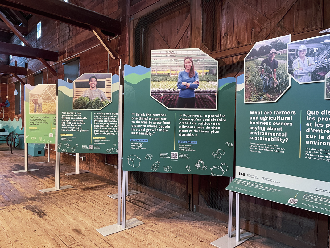 Four exhibition panels, with quotes and images of agriculture workers. They are on display in a wooden barn.