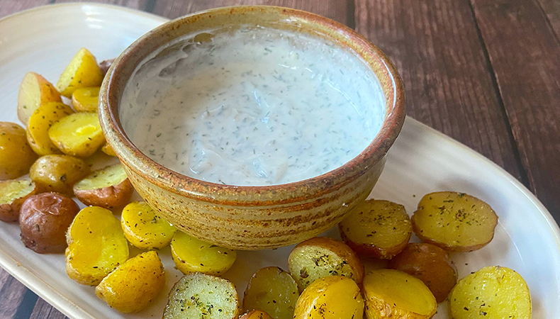 Un bol de sauce repose au centre d'un plateau blanc entouré de pommes de terre rôties.