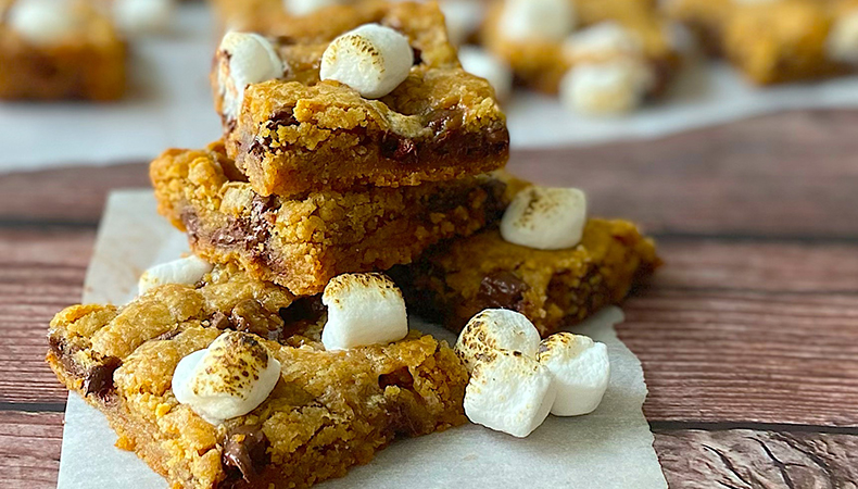 Plusieurs barres de s'mores sont posées sur un petit morceau de papier parchemin sur une surface en bois. D'autres barres sont visibles à l'arrière-plan.