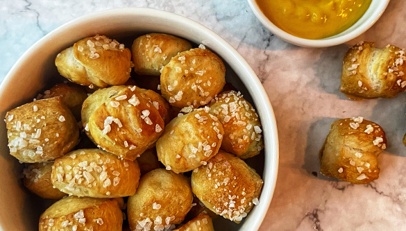 Vue aérienne en gros plan d'un petit bol rempli de bretzels, posé sur un comptoir en marbre. Un plat de moutarde et quelques bouchées de bretzel sont posés à côté du bol.