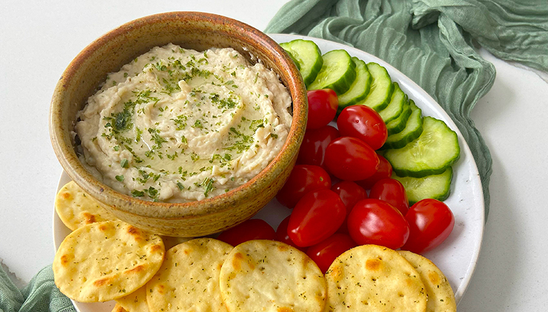 Une vue aérienne montre un plateau coloré de légumes et de chips de pita, ainsi qu'un bol de sauce.