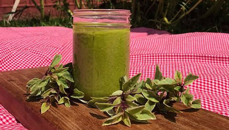 Un pot de liquide vert est posé sur une planche à découper, à côté de brins de basilic.