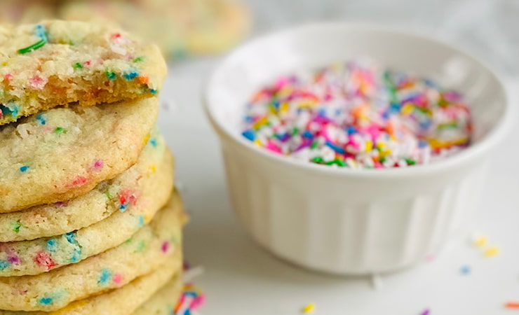 Un biscuit est posé sur une surface blanche. À côté, une pile de biscuits et un bol rempli de paillettes.