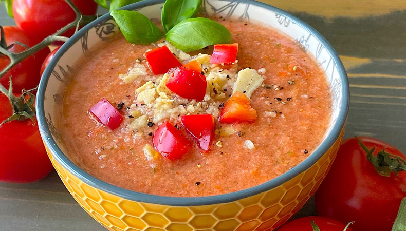 A bowl of gazpacho garnished with diced tomatoes and red peppers, fresh basil and croutons.