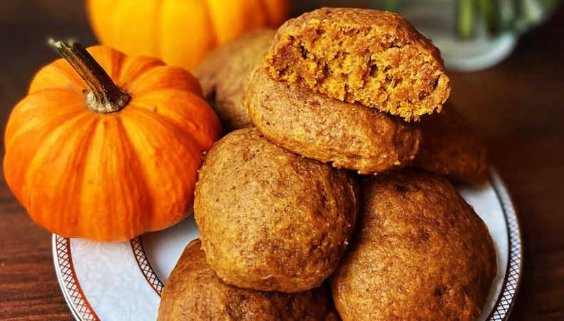 Une petite pile de biscuits marron à la citrouille est disposée sur une assiette, à côté de quelques citrouilles miniatures.