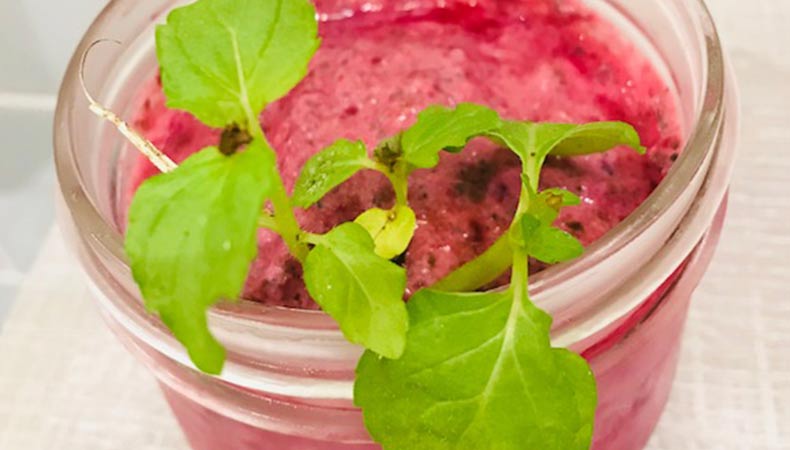 A glass of thick, pink strawberry smoothie. It is garnished with fresh mint.