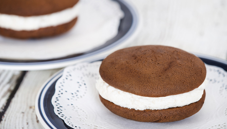 Un sandwich fait de biscuits au chocolat et de crème glacée à la vanille disposé sur un napperon dans une petite assiette. On peut voir un deuxième sandwich en arrière-plan.