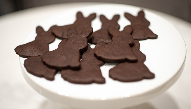 Des biscuits brun foncé en forme de lapin sont présentés sur un plateau blanc surélevé.