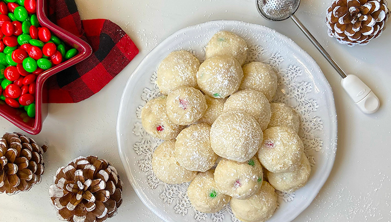 Une vue aérienne d’une assiette de biscuits ronds blancs. On peut voir des cocottes, un ustensile de cuisine et un plat de bonbons près de l’assiette.