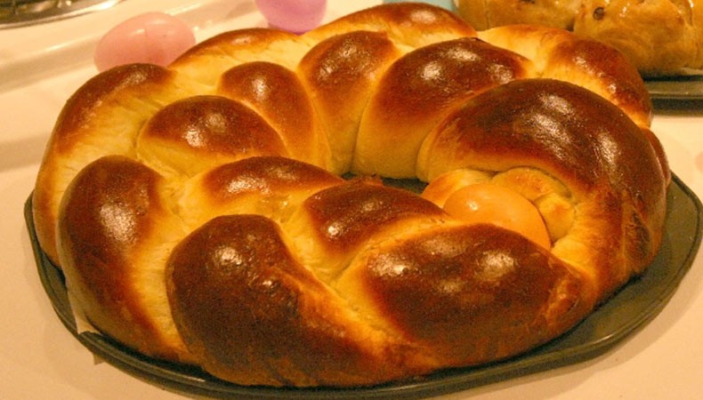 A golden, brown, braided bread. This circular bread has a hole in the middle, and sits upon a round baking sheet.