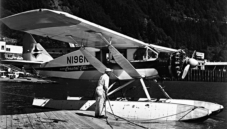 Photo en noir et blanc d'un avion Bellanca CH-300 Pacemaker flottant sur un plan d'eau à côté d'un quai.