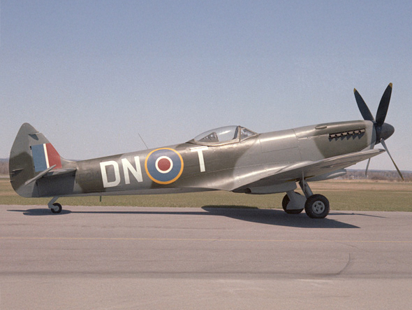 Un avion à hélices camouflé est posé sur une piste. Il porte les lettres DNT sur son flanc, à côté d'un emblème circulaire.