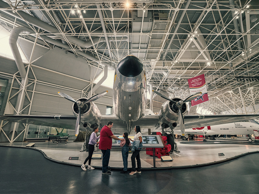 Several people gather near the exhibition panel in front of the large DC-3 aircraft.