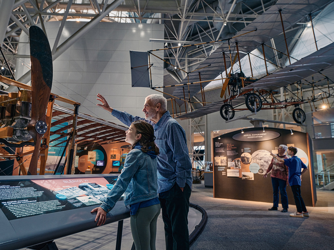 A young child and an older person look at an exhibition of early aircraft