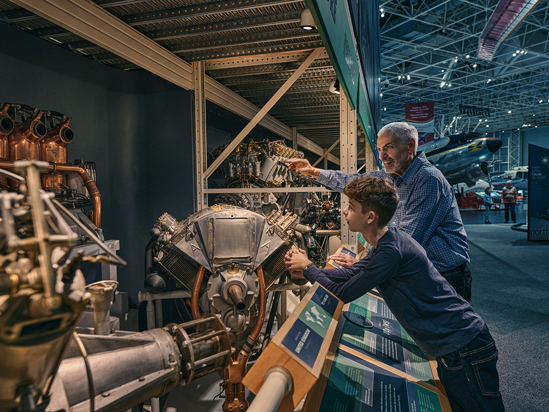 A man and a younger child look at an engine on display in the museum.