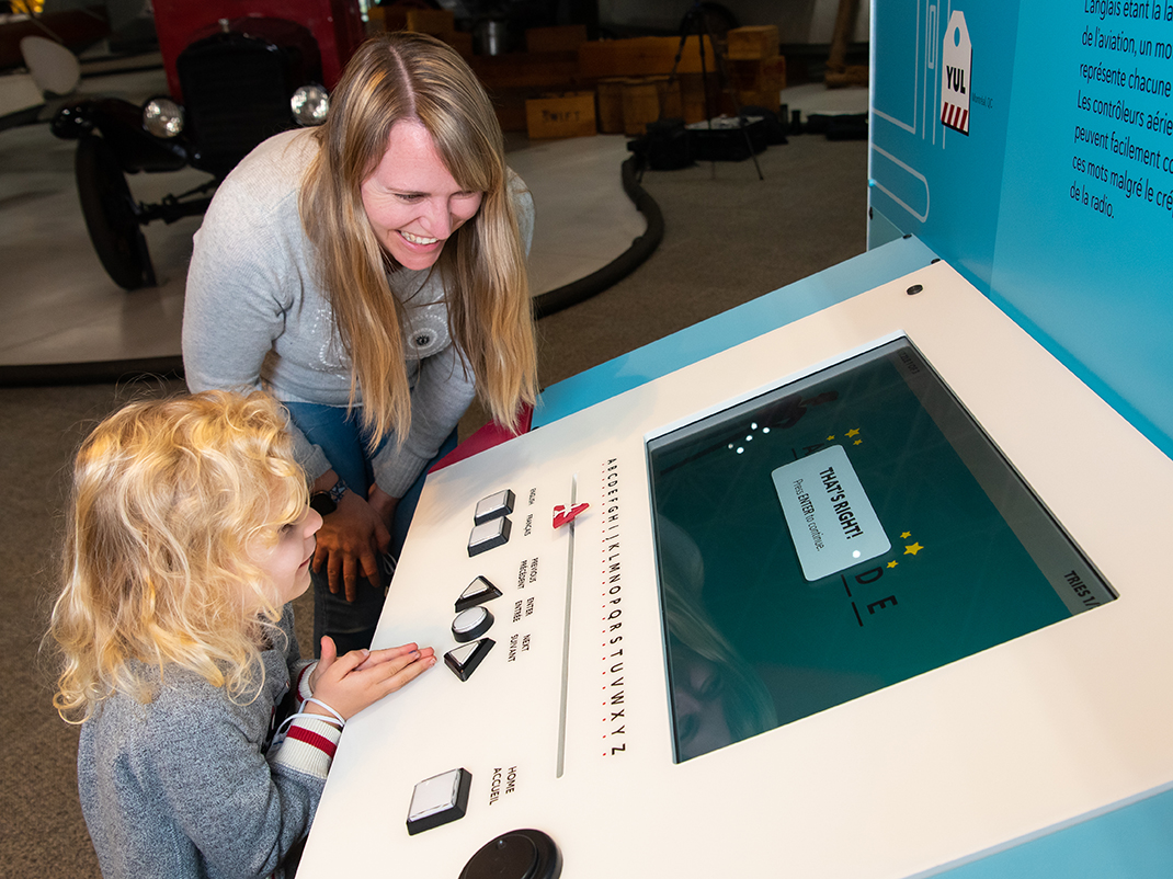 An adult and child smile at an interactive console in the museum's Eyes on the Skies exhibition.