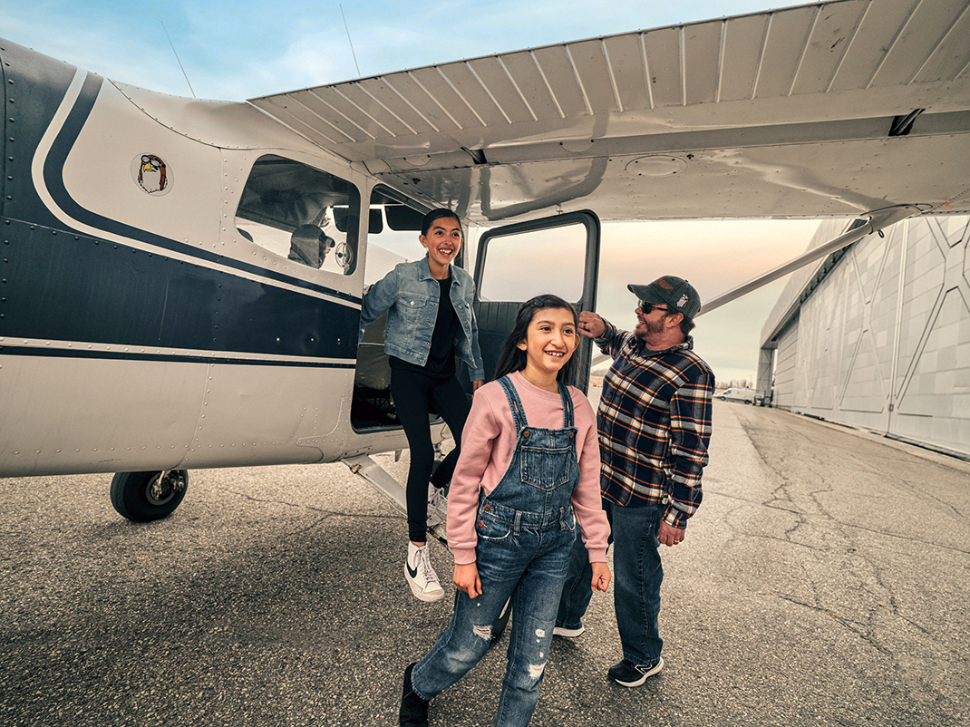 Two adults and a young person climb out of a Cessna aircraft on the runway outside the museum