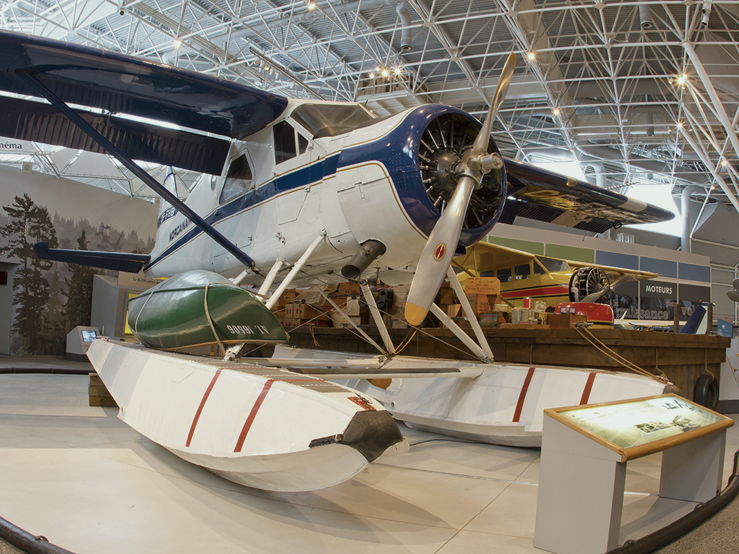 A float plane, with white pontoons, a white body with blue striping, blue wings and a long propellor.