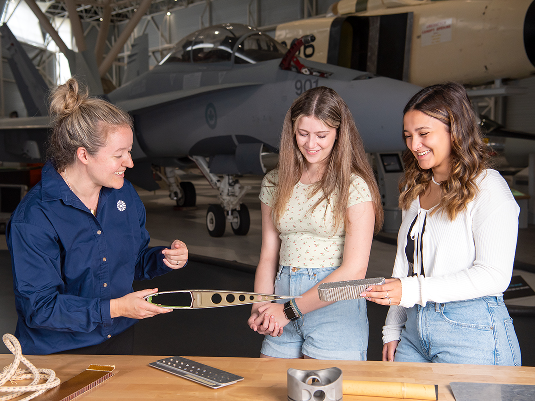 Two high school students examine material used to make aircraft on a tabletop. In the background there is a historic fighter jet.