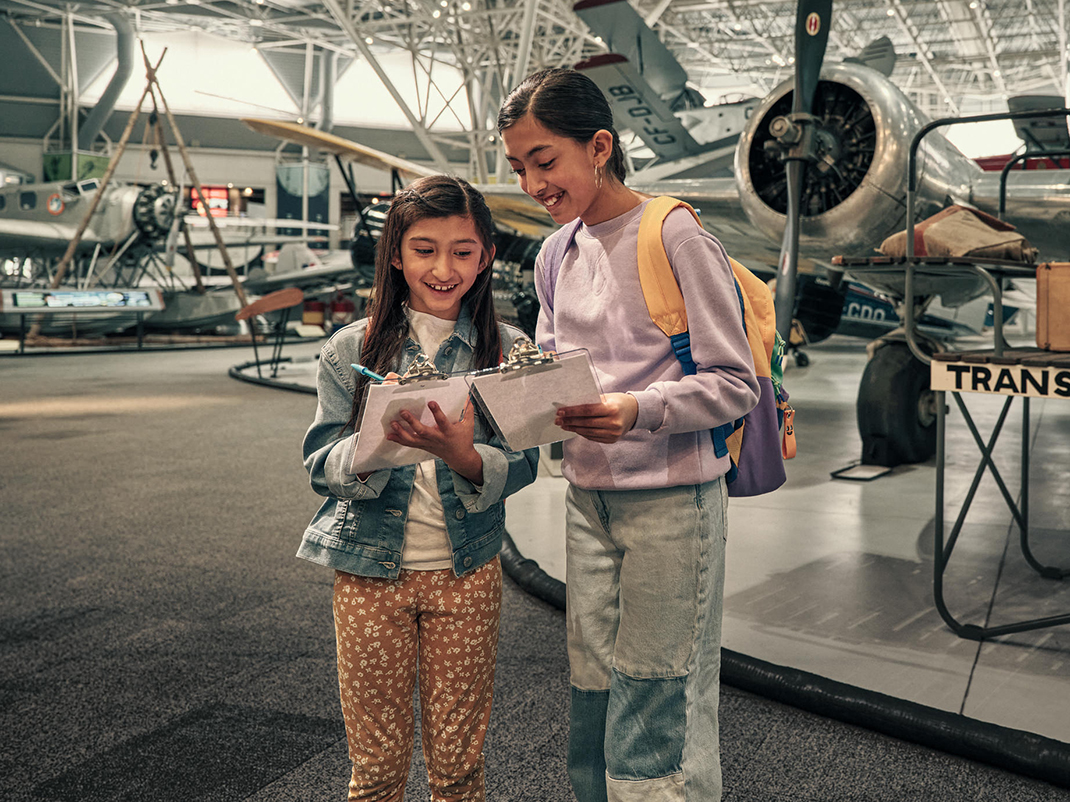 A group of students smiles at the camera. They are gathered at the Canada Aviation and Space Museum, with historic aircraft in the background.