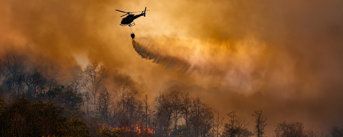 Un hélicoptère vole dans un ciel enfumé et largue un liquide sur un feu de forêt.