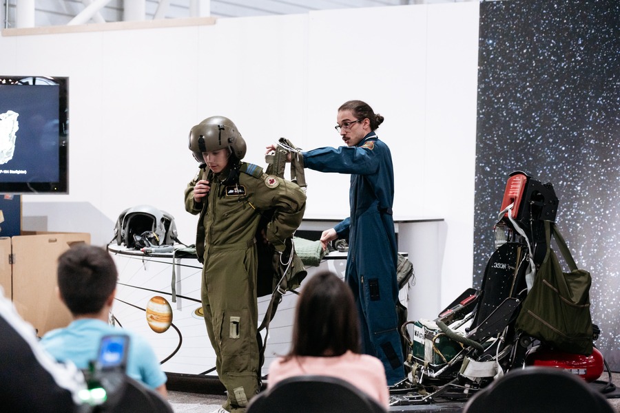 A guide helps a visitor into a jet pilot outfit