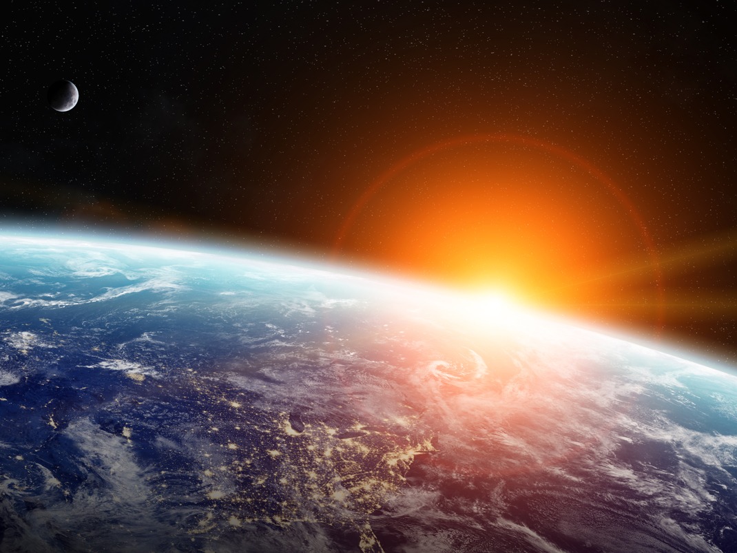 Vue d'une partie de la Terre depuis l'espace, où le Soleil se lève à peine et est entouré d'une lumière orange.