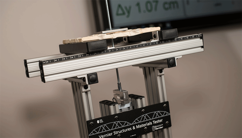 Weighted materials in the form of a prototype bridge lie across a large metallic scale