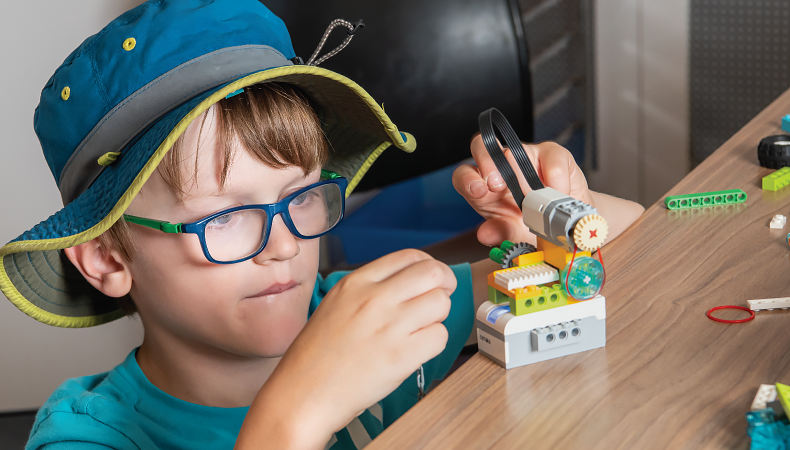 A young child wearing a blue hat and glasses plays with building materials.