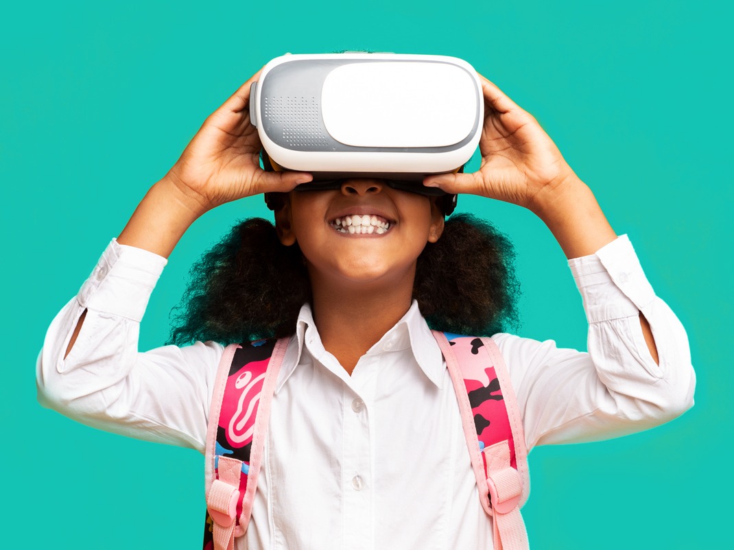 Un enfant portant un sac à dos tient un casque de réalité virtuelle devant ses yeux, sur un fond turquoise uni.