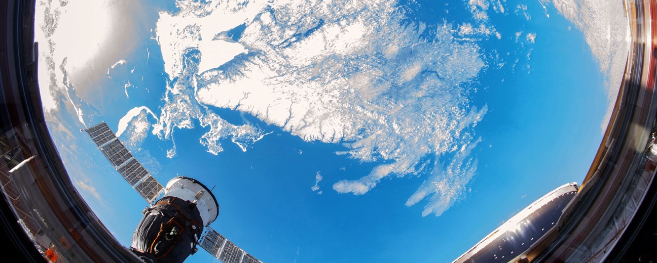 Vue de la Terre depuis l'espace montrant Terre-Neuve et les formations nuageuses environnantes, capturée à travers une fenêtre circulaire d'un vaisseau spatial avec une partie de la structure d'un satellite et d'une station visible dans le cadre.