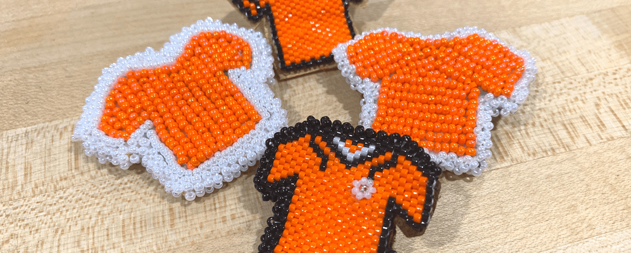 Four orange T-shirts decorated with beadwork, displayed side by side.