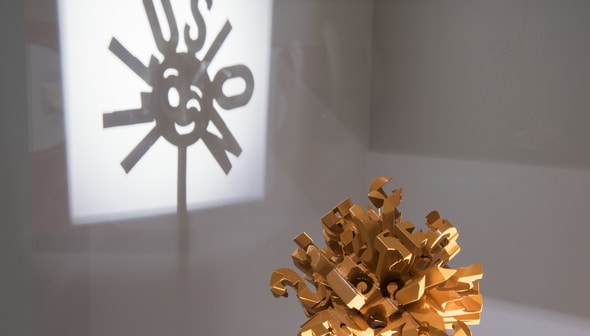 A sculpture is shown in the foreground, with its shadow in the background. The shadow spells "illusion"