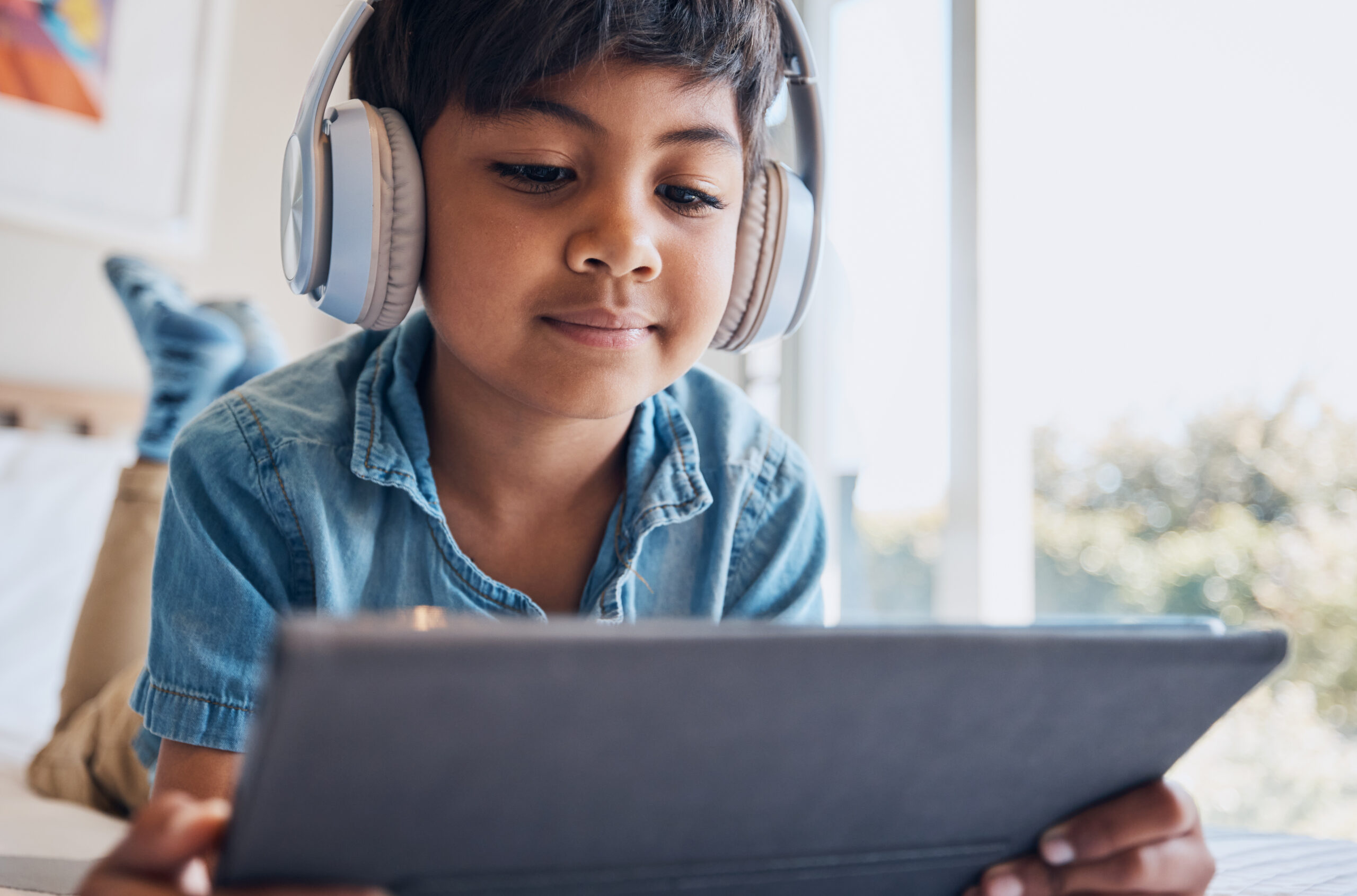 A child with headphones looks intently at a tablet screen