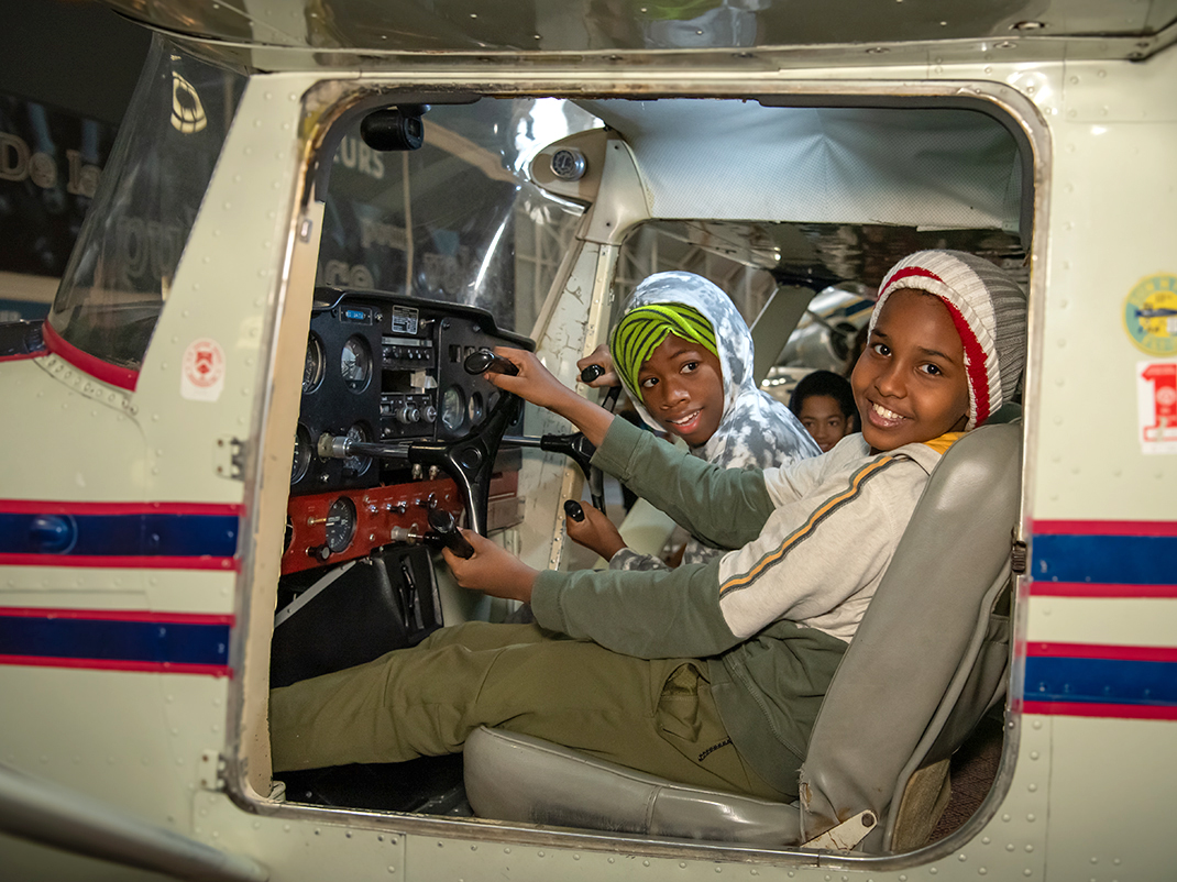 Two children smile, sitting in the cockpit of an aircraft.