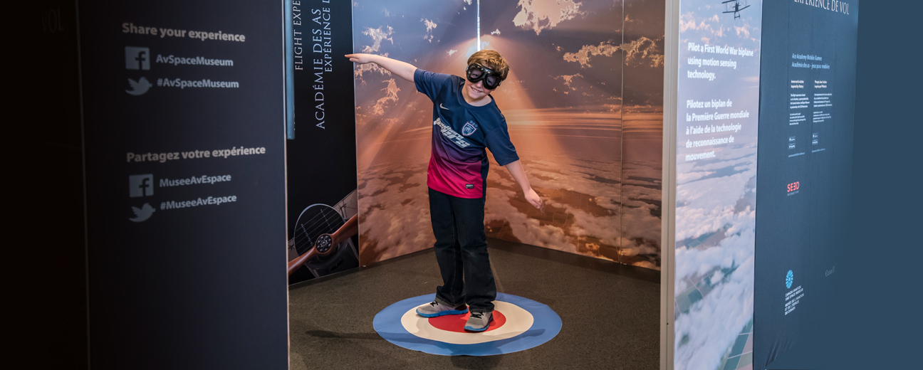 A kid with short hard wearing a blue shirt standing in the middle of the Ace Academy exibition looking down with arms out like an airplane. The kid is surrounded my multiple panels with text and images of clouds.