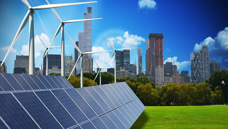 Two rows of solar panels sitting on a green lawn, in behind them are six wind turbines. In the background there is a cityscape with tall skyscrapers and a line of trees in front of it.