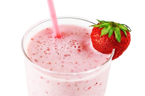 A glass is filled with a pink smoothie, with a strawberry garnishing the rim.