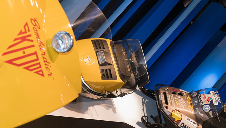 Three yellow Ski Doo snowmobiles on display in a museum exhibition