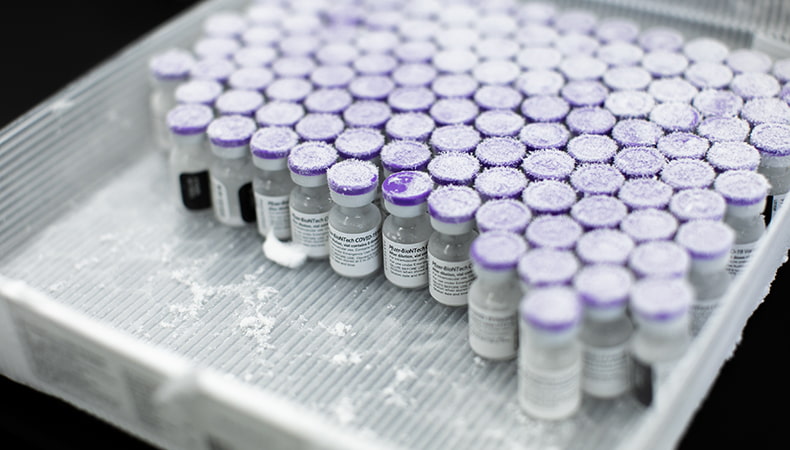 Dozens of tiny vials of vaccine sit side-by-side in a square tray