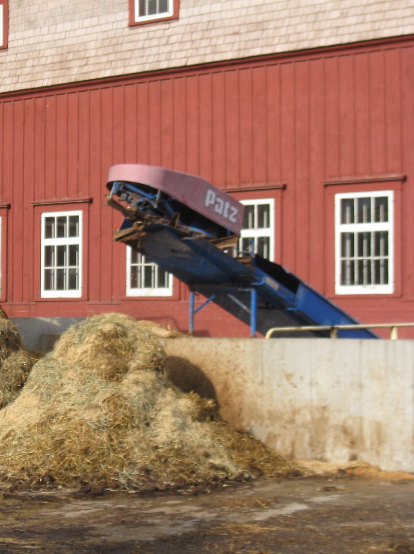 A photo on the exterior of the barn showing the conveyer belt system with a pile of waste.