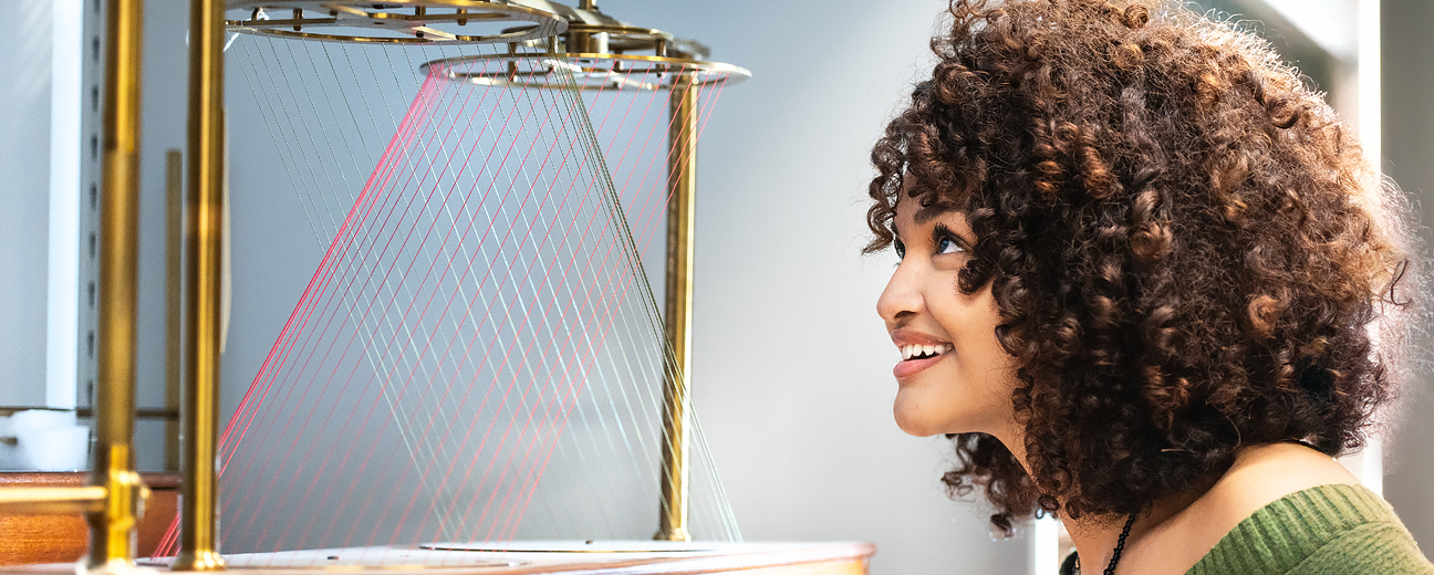 Femme noire aux cheveux bouclés regardant avec intérêt un objet de collection représentant un modèle mathématique