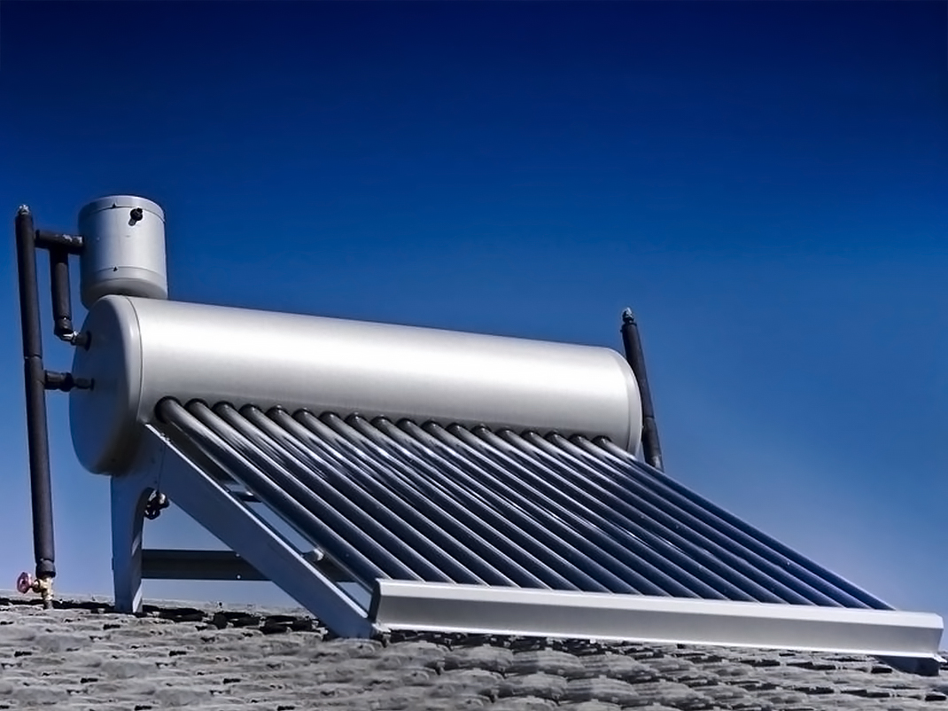 A solar water heater with a large tank and several tubes jutting out to one side sits on the roof of a building.