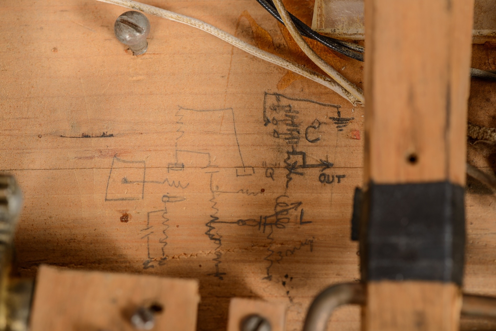 A piece of old pine used as the frame for the Electronic Sackbut with an electronic schematic drawn in pencil in the middle of the image. The schematic is surrounded by wires, screws, and other pieces of wood and metal hardware.
